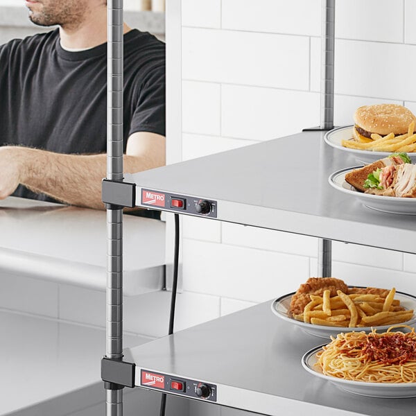 A man in a black shirt sits at a table with a cheeseburger and fries on a Metro Super Erecta heated shelf.