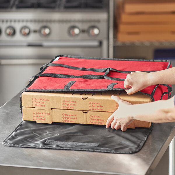 A person putting a pizza box into a red Choice insulated pizza delivery bag.