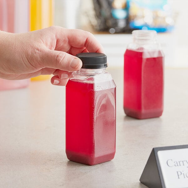 A hand holding an 8 oz. tall square PET clear juice bottle filled with red liquid.