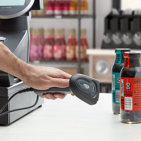 A person using a Royal barcode scanner to scan a red beverage bottle at a convenience store counter.