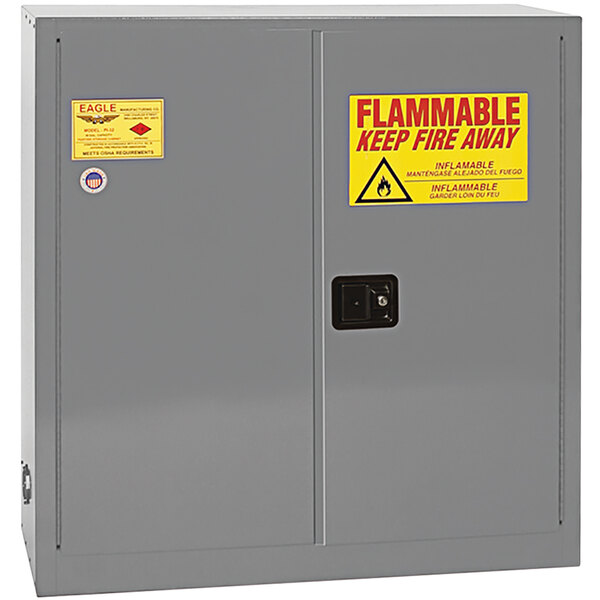 A grey metal Eagle Manufacturing safety cabinet with a yellow and red flammable sign.