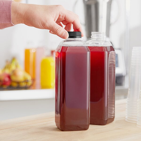 A hand pours red juice into a square PET juice bottle on a counter.
