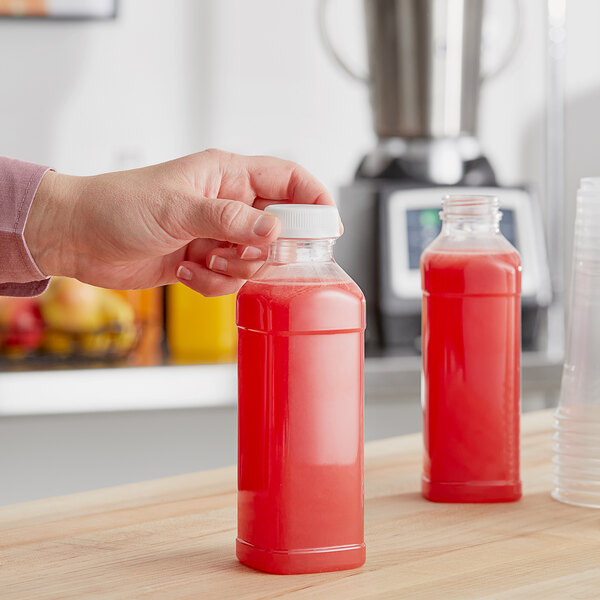 A hand holding a Square PET clear juice bottle filled with red liquid.