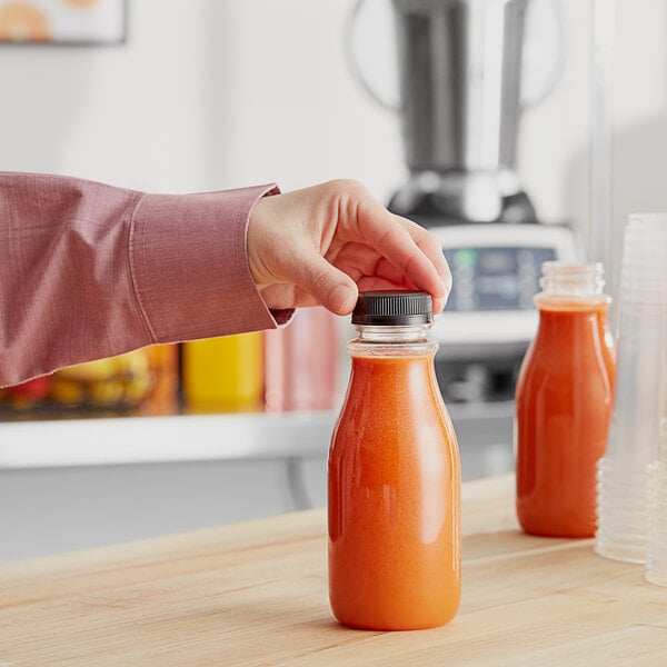 A hand pouring orange juice into a clear PET juice bottle with a black lid.