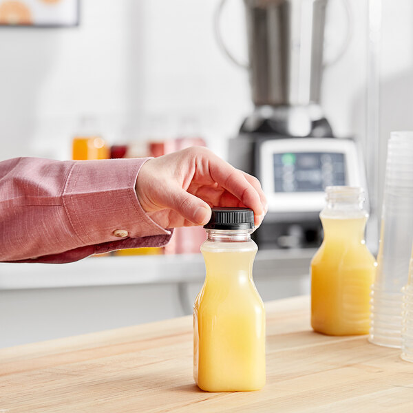 A hand pouring orange juice into a clear plastic square carafe bottle.