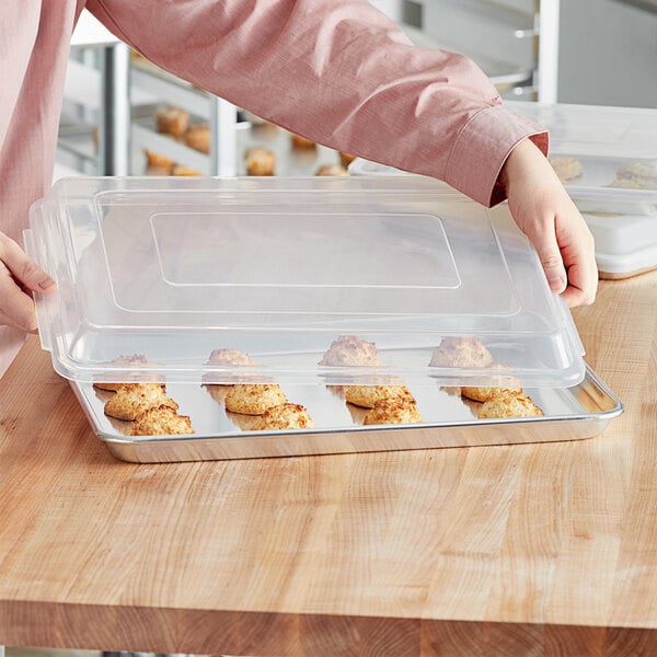 A woman's arm reaching out to a clear plastic Choice bun pan cover filled with cookies.