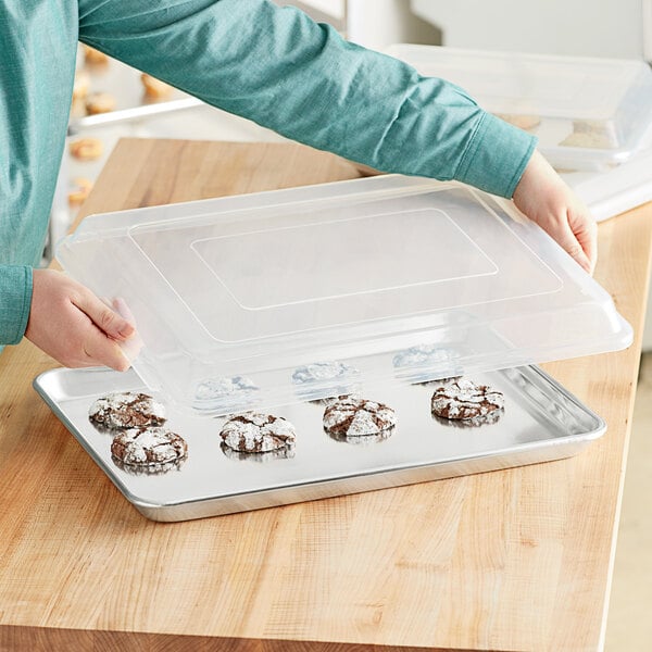 A person holding a Choice aluminum sheet pan with cookies.