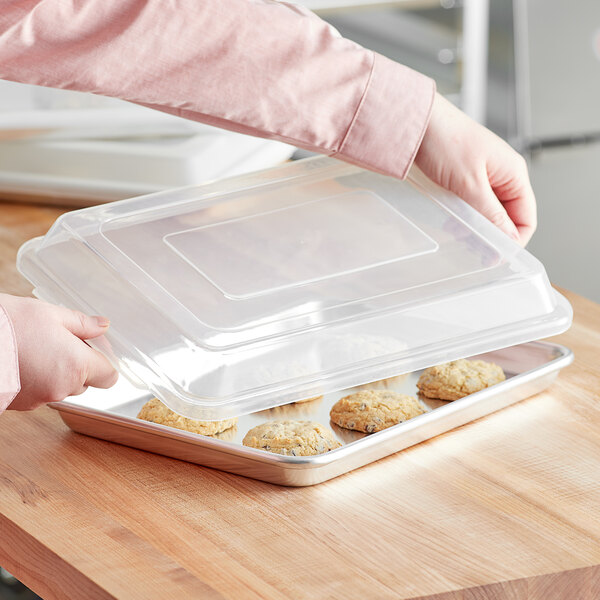 A hand putting a Choice polypropylene bun cover on a tray of cookies.