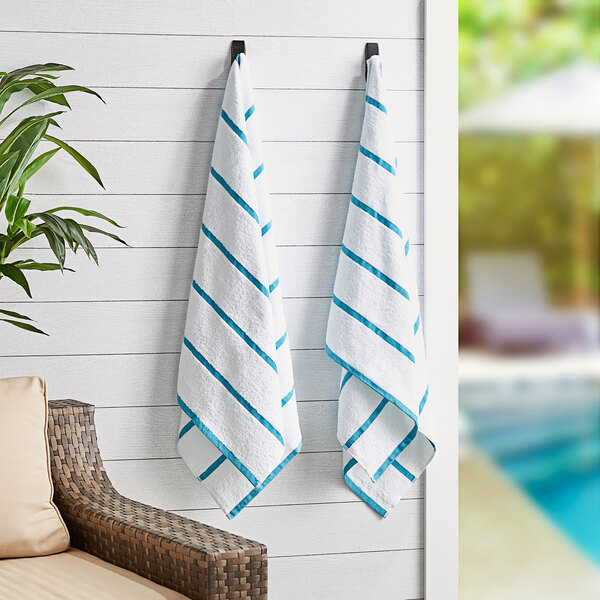Two Monarch Brands Las Rayas pool towels with blue stripes hanging on a wall.