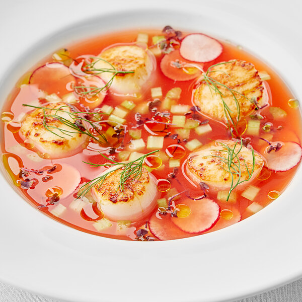 A bowl of soup with scallops and a close up of a fruit.
