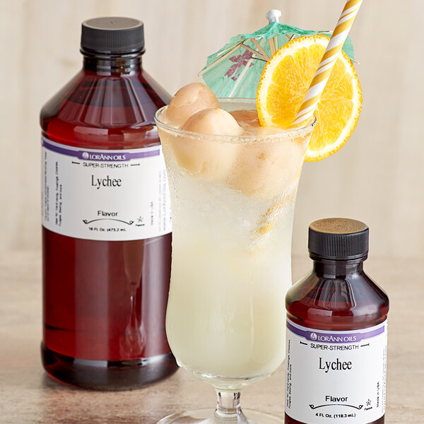 A bottle of LorAnn Oils Lychee Super Strength Flavor on a white background with a glass of lychee-flavored liquid with ice and a straw.