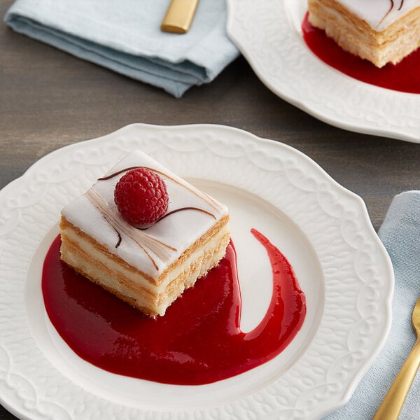 A slice of cake with a raspberry on top on a white plate.