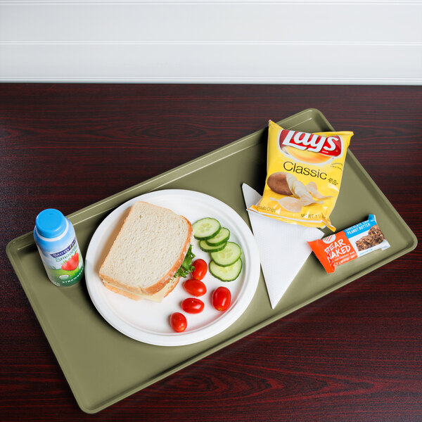A tray with a plate of food including a sandwich and vegetables on it.