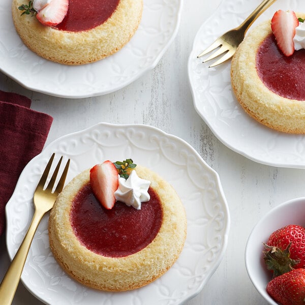 A group of strawberry desserts on white plates with gold forks.