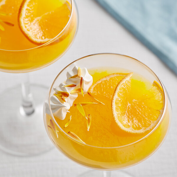 Two glasses of Les Vergers Boiron Corsican Clementine fruit puree with orange slices and whipped cream.