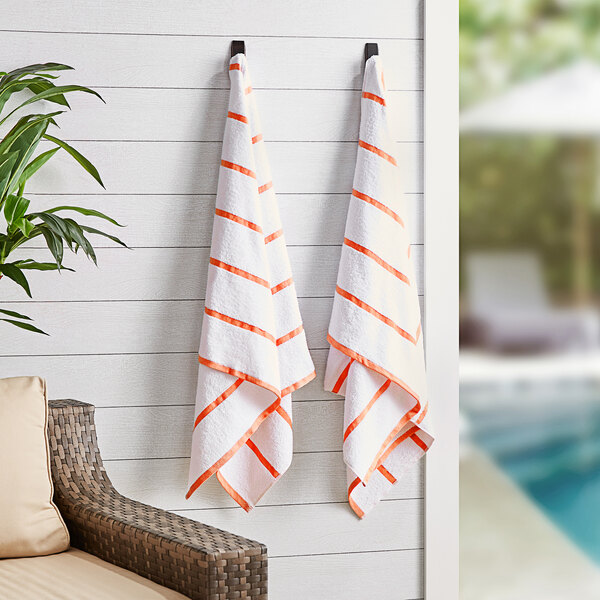 Two Monarch Brands orange striped pool towels hanging on a wall.