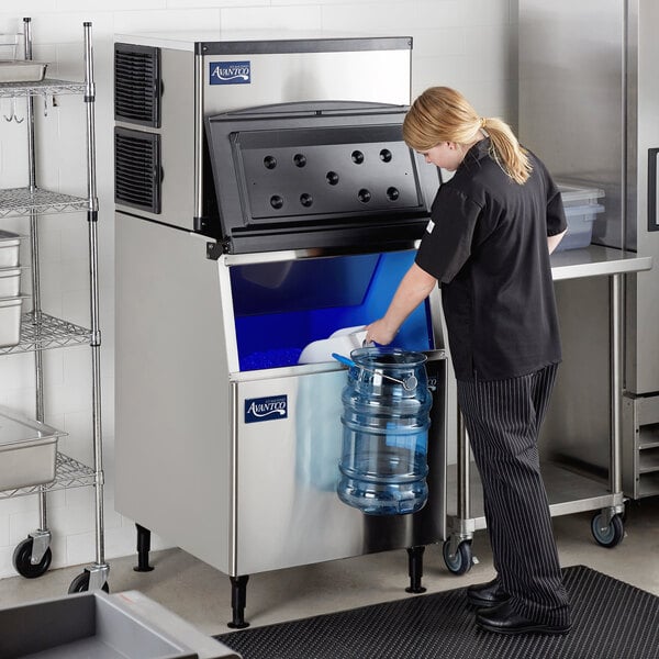 A woman standing in a school kitchen pours water into an Avantco Air Cooled Modular Half Cube Ice Machine.