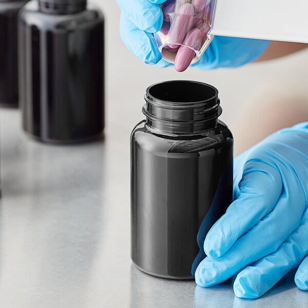 A person in blue gloves holding a dark amber 225cc packer bottle filled with black liquid.