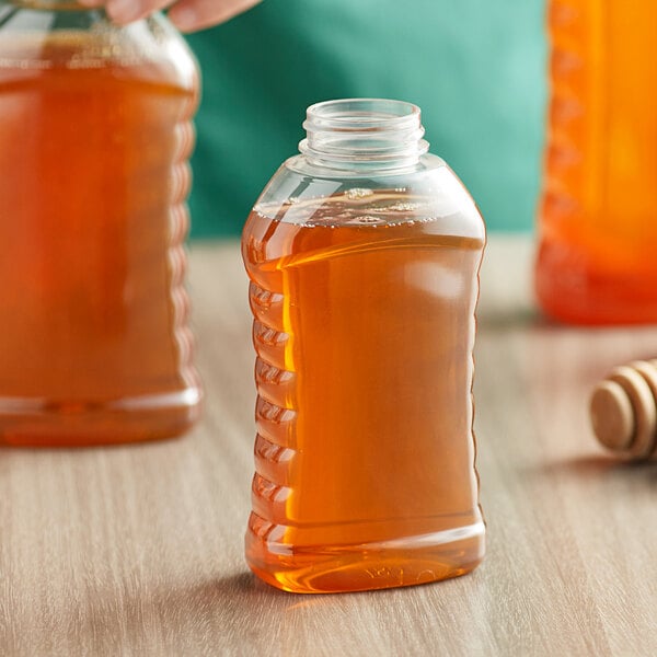 A person holding a ribbed hourglass PET honey bottle filled with liquid.