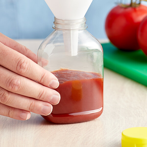 A hand pouring ketchup into a yellow round PET sauce bottle.