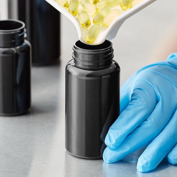 A person in blue gloves pouring yellow pills from a black can into a dark amber 150cc packer bottle.
