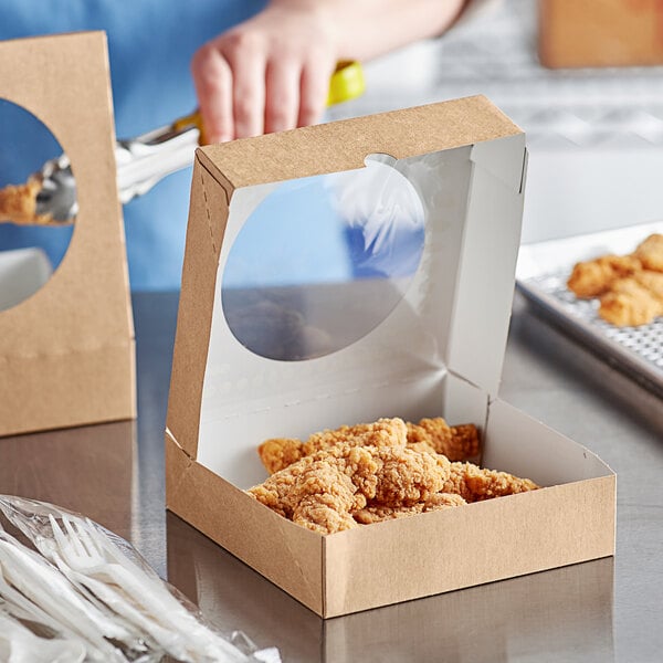 A hand cutting up chicken in a Kraft paper take-out box with a window.