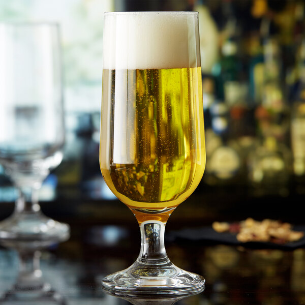 Two Anchor Hocking stemmed pilsner glasses filled with beer on a table.