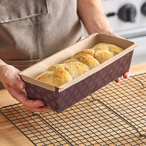 A person holding a Novacart corrugated kraft paper bread loaf pan filled with bread.