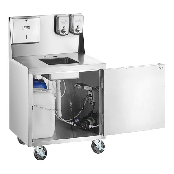 A stainless steel portable hand sink cart with a single bowl, paper towel dispenser, two soap dispensers, and an open cabinet showing water containers and plumbing components, all mounted on wheels.