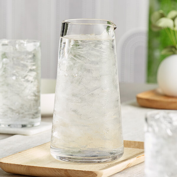An Acopa Pangea glass carafe filled with ice water on a wooden tray.