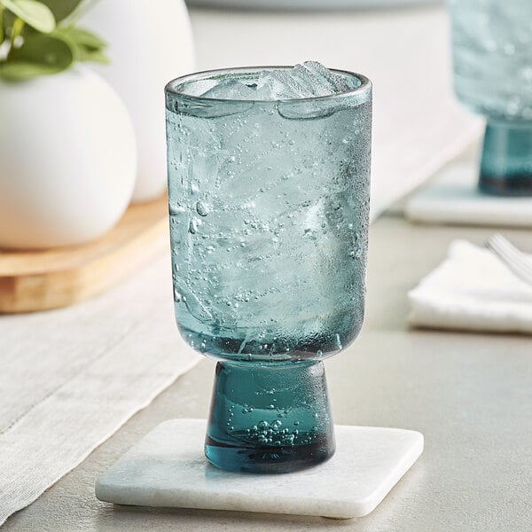 An Acopa blue goblet filled with ice water on a coaster.