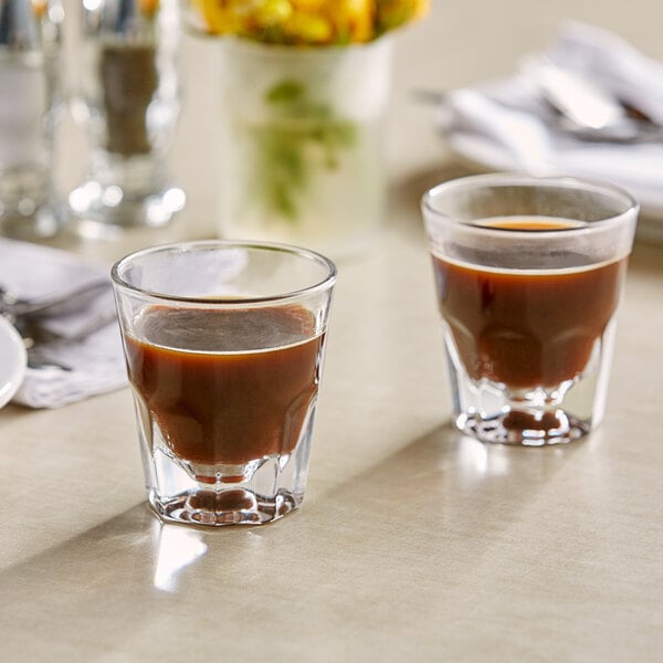 Two Acopa Memphis espresso glasses filled with brown liquid on a table.