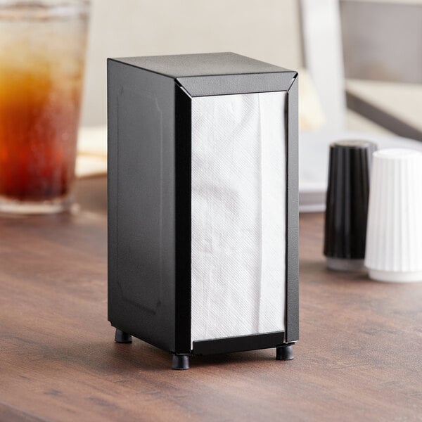 A black Choice tabletop napkin dispenser with white napkins on a table.