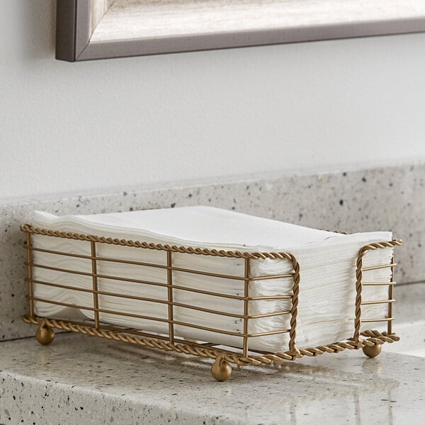 A bronze metal Hoffmaster guest towel holder on a counter holding napkins.