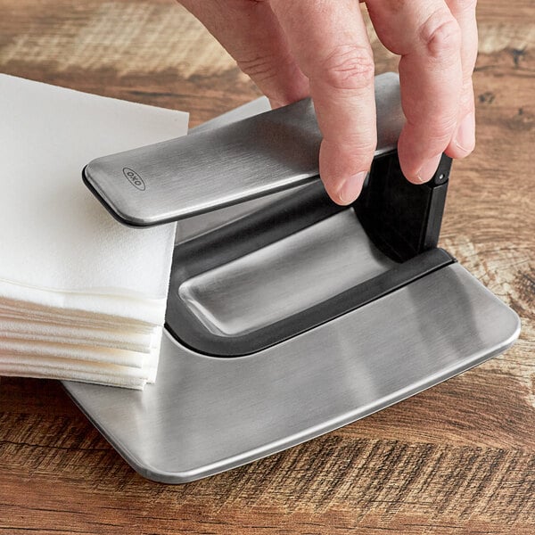 A hand using the OXO SimplyPull napkin holder to wipe a table.