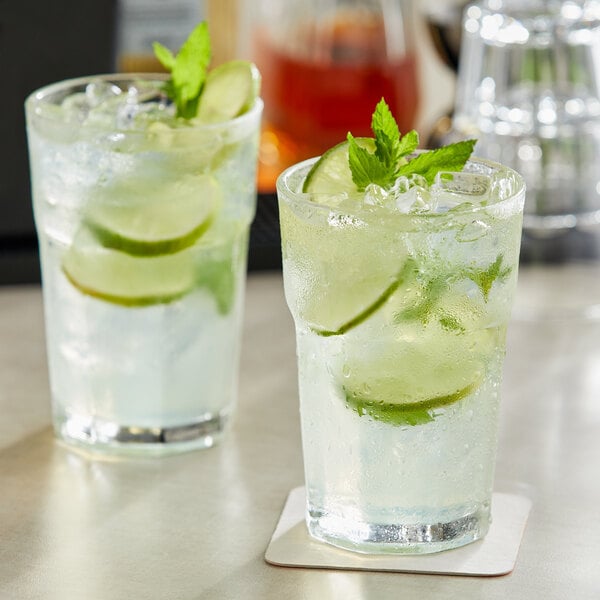 Two Acopa Memphis beverage glasses with ice and cucumber drinks.