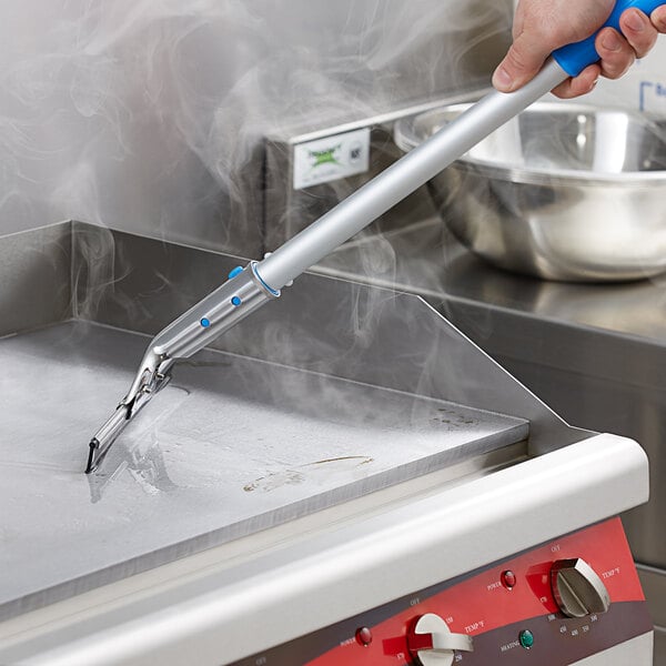 A person using a Scrubble by ACS griddle squeegee to clean a griddle.