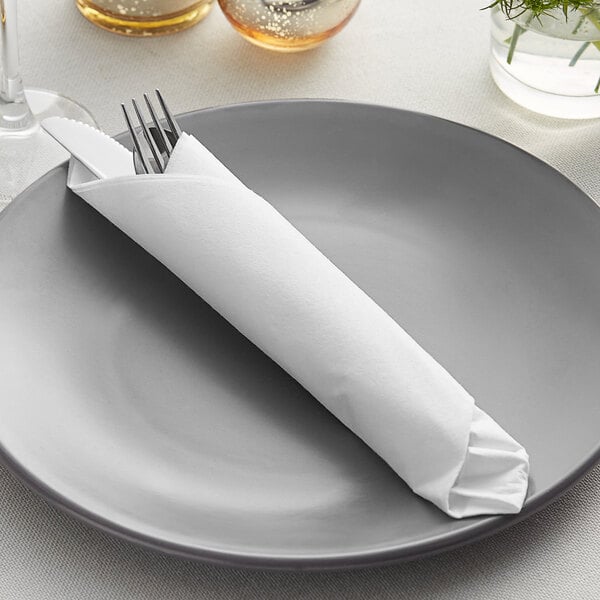 A Hoffmaster white linen-like dinner napkin wrapped around silverware on a plate.