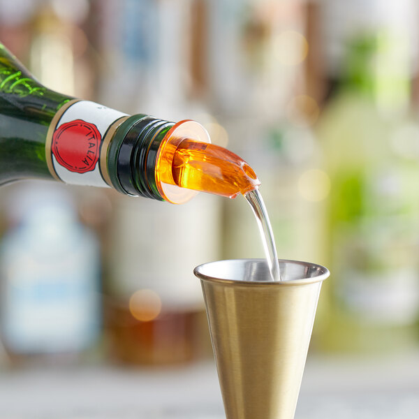 A bottle pouring liquid into a metal cup using a Choice Short Free Flow Amber Liquor Pourer.