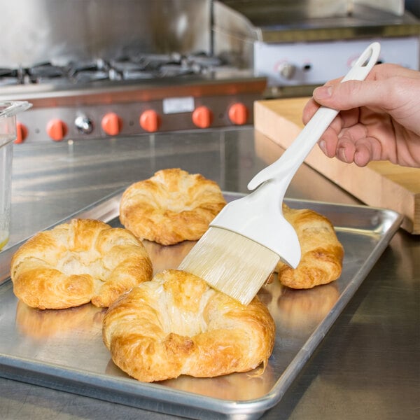 A person using a Winco boar bristle pastry brush to brush pastry onto a tray.