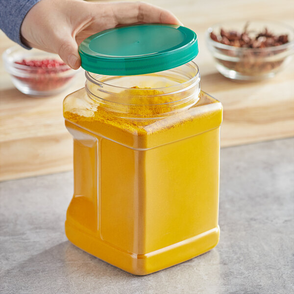 A person holding a 64 oz. Square PET plastic jar with a green lid filled with yellow liquid.