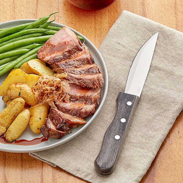 An Acopa steak knife with a jumbo gray pakkawood handle on a napkin next to a plate of meat and potatoes with green beans.