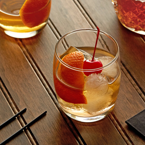 A glass of Master of Mixes Old Fashioned drink with ice, orange, and a cherry.