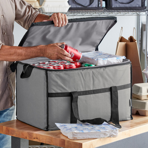 A person putting a red soda can into a large gray Choice insulated cooler bag.