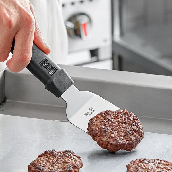 A hand holding a Choice mini turner with a black handle flipping meat patties.