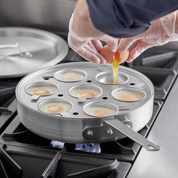 A person putting eggs into an egg poacher pan on a stove.