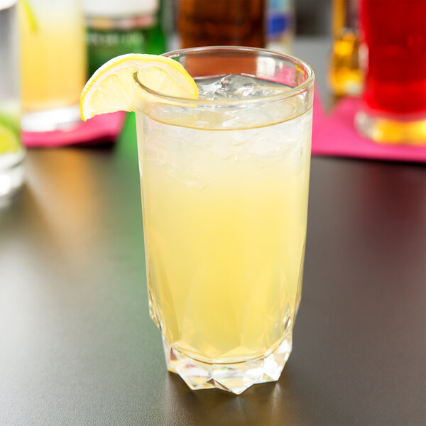 A glass of yellow liquid with ice and a slice of lemon on the rim.