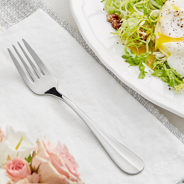An Acopa Brigitte stainless steel salad fork on a white plate with food.