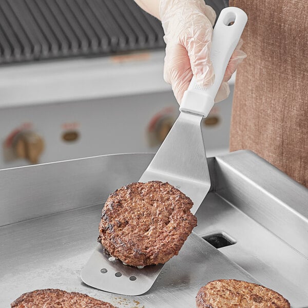 A person using a Choice perforated turner to flip a burger on a grill.