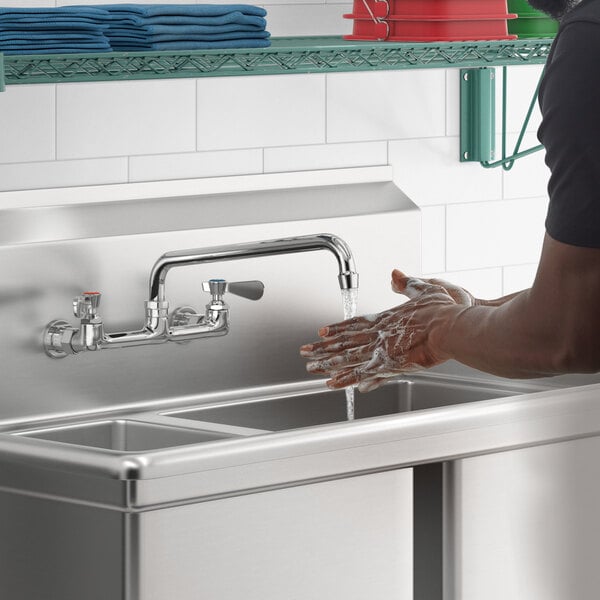 A man washing his hands in a stainless steel sink using a Regency wall mount faucet.